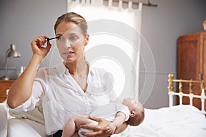 Working Mother Holding Baby And Putting On Make Up