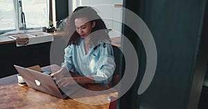 Working online. Beautiful young smiling African American business woman typing message on laptop at home kitchen table.