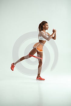 Working out. Full length of young african woman with beautiful body doing exercises with resistance band in studio