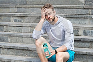 Working out on stairs. Man athletic appearance exhausted holds water bottle. Man athlete sport clothes refreshing