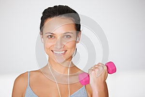 Working out to the rythm. Portrait of a young woman working out with weights while listening to music.