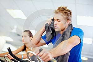 Working out. Young man tired while cycling at the gym.