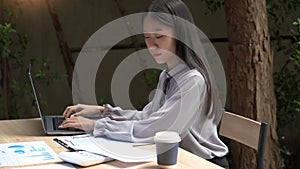 Working outdoor concept a young woman typing on the laptop with a cup of coffee outside the building surrounded by relaxing