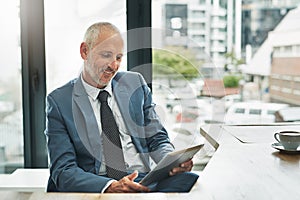 Working in a paperless office to match a modern business. a mature businessman working on a digital tablet in a modern