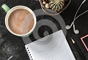 Working place with open notebook  and pencil, coffee cup, headphones, music player and cactus on the black background desk. workin