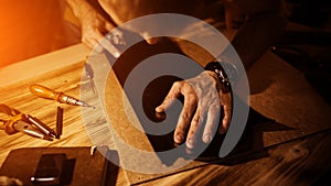 Working process of the leather belt in the leather workshop. Man holding tool. Tanner in old tannery. Wooden table photo