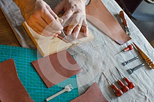 Working process in the leather workshop. Man holding crafting tool and working. He is sewing to make a walet. Tanner in