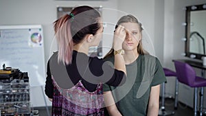 Working process of make-up applying at beauty studio. Professional expert is setting powder on girl`s face. Blonde young