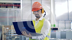 Working process of a male factory worker in protection workwear with a laptop