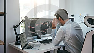 Working process. Smart male trader looking at charts on multiple computer screens and analyzing data while sitting in