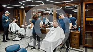 Working process. Three professional barbers serving clients in the modern loft style barbershop