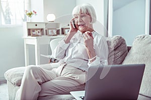 Working retired woman calling her business partner sitting near laptop