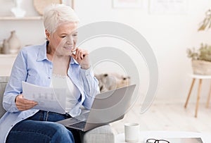 Working On Retirement. Elderly Woman Holding Papers And Using Laptop At Home