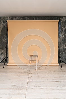 The working space of the photo studio with a beige paper background and chair.