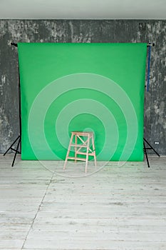 The working space of the photo studio with a green paper background and chair.