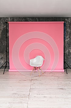 The working space of the photo studio with a pink paper background and chair.