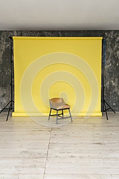 The working space of the photo studio with a yellow paper background and chair.