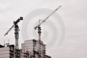 Working tall cranes inside place for with tall buildings under construction against a clear blue sky. Crane and building working