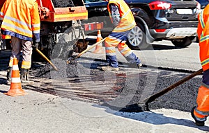 Working team levels the fresh asphalt with shovels on a repaired area in road construction