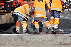 A working team of road workers in an orange uniform scatters a part of the asphalt with shovels to repair a section of the road