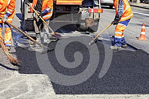 The working team smoothes hot asphalt with shovels by hand when repairing the road