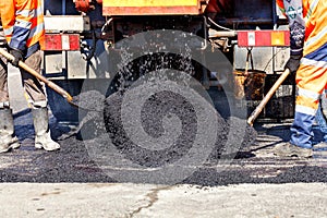 The working team sprinkles part of the asphalt with shovels to update it in road construction