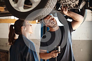 Working together to decide the best course of action. two mechanics working under a car in an auto repair shop.