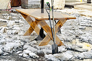 working tool for clearing snow and ice left near wooden table on the site of a street cafe