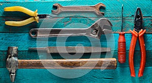 Working tool on a turquoise wooden background: screwdriver, pliers, scrap, hammer, nippers, file, adjustable wrench.