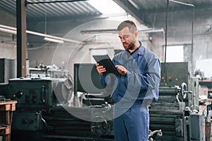 Working by using digital tablet. Man at the factory that is in blue uniform is indoors