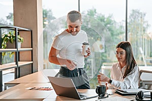 Working by using laptop. Man and woman are in the modern office together