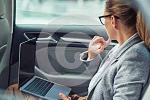 Working on the way to the office, side view of a thouthfull caucasian business woman working on laptop while sitting on