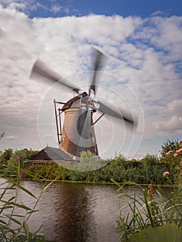 Working windmill on the coast of the river against a cloudy sky in Kinderdijk