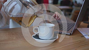 working woman cafe pouring hot tea from transparent teapot into white cup, drink