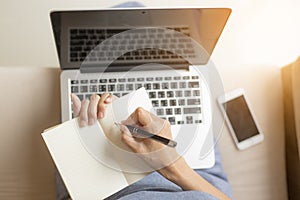 Working women holding a pens writing a notebook.She works using laptop.