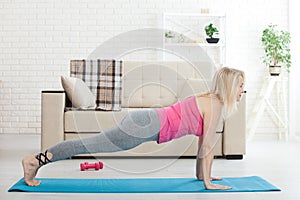 Working with your body. Full length of beautiful middle aged woman in sportswear doing plank while standing in front of window at