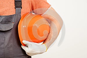 Workman holding orange helmet close up. Worker in a construction site. Builder wearing a protective glove