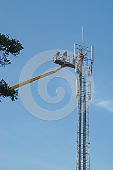 Workman in an hydraulic hoist repairing installation of a high telephonemast