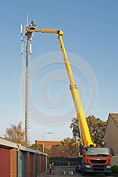 Workman in an hydraulic hoist repairing installation of a high telephonemast