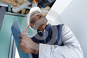 workman looking at ventilation system and making notes on clipboard photo