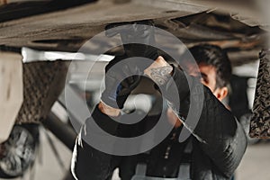 Workman mechanic working under car in auto repair shop