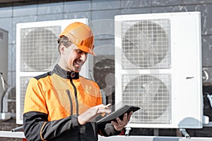 Workman servicing air conditioning or heat pump with digital tablet