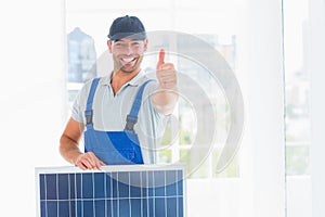 Workman with solar panel gesturing thumbs up in bright office