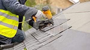 Workman using pneumatic nail gun install tile on roof of new house under construction