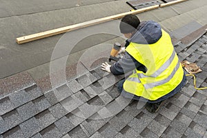 Workman using pneumatic nail gun install tile on roof of new house under construction