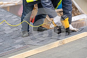 Workman using pneumatic nail gun install tile on roof of new house under construction