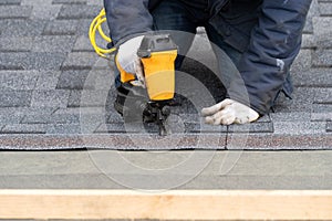 Workman using pneumatic nail gun install tile on roof of new house under construction