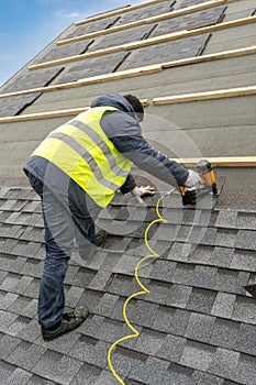 Workman using pneumatic nail gun install tile on roof of new house under construction