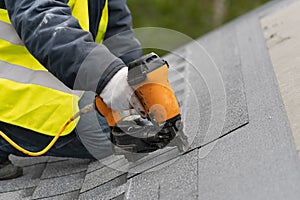 Workman using pneumatic nail gun install tile on roof of new house under construction