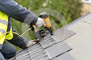 Workman using pneumatic nail gun install tile on roof of new house under construction